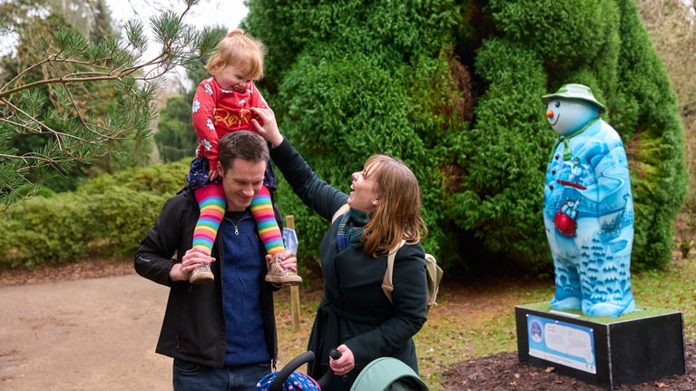 A family laugh and share a moment in front of a Snowman sculpture in the gardens.